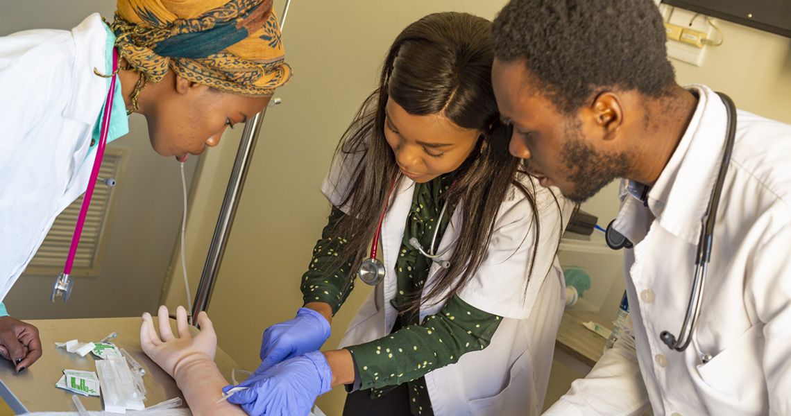 Three medical students learning how to insert a needle in an arm